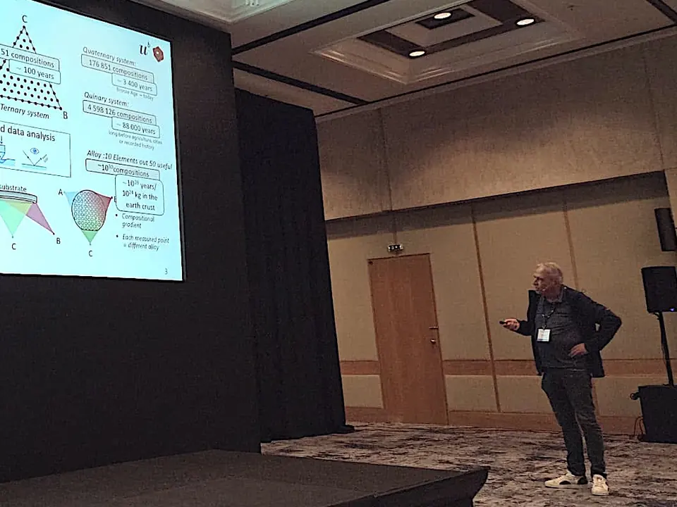 Johann Michler presenting beside a slide on combinatorial sputtering, where each measured point on a wafer is a different alloy